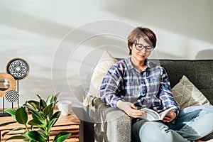 Woman in eye glasses sit on the sofa and relax while reading a book at home in cozy modern interior living room with