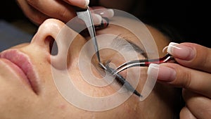 Woman eye with long eyelashes. Eyelash extension. Gluing artificial eyelashes with tweezers. A woman lies under a lamp