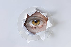 Woman eye observes through a hole in the paper photo