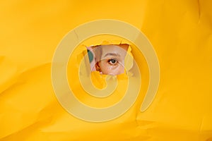 Woman eye peeking through a hole in a big sheet of cramped yellow paper
