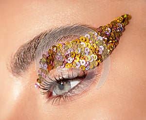 Woman eye with yellow sequins makeup closeup