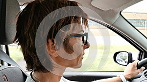 Woman with eyeglasses driving car with hands on steering wheel. Interior close up, side view, traffic on street. Vintage filter, t
