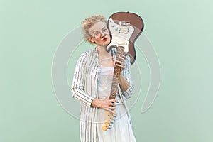 Woman with eyeglasses holding electric guitar, looking at camera with raised eyebrow.