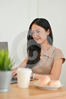 Woman with eyeglasses sits in her office workspace, typing on keyboard notebook
