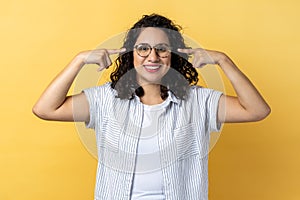 Woman in eyeglasses, standing pointing at her new spectacles, looking at camera.