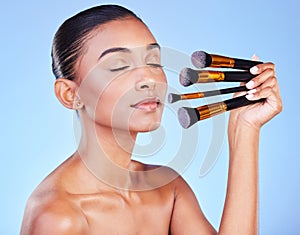 Woman, eyes closed and beauty, makeup and brush for foundation with cosmetics isolated on blue background. Indian model