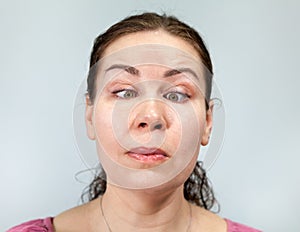 Woman with eyes slanted to her nose, crossed eyes, craziness, portrait on grey background, emotions series photo