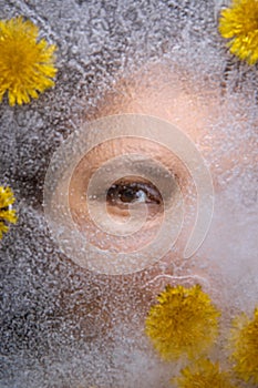 Woman eyes  through  ice with dandelions flowers