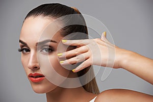 Woman face, beauty and hand with manicure, makeup and yellow nail polish, skin and cosmetics on grey background. Orange