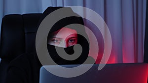 Woman face in black mask and hoodie looking at computer screen and breaking password. Young hacker breaks security protection on l