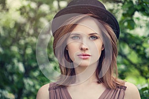 Woman face closeup outdoor portrait. Pretty girl in hat on greenery foliage background