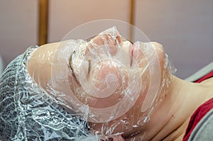 Woman face covered with plastic wrap in beauty salon