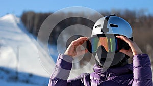 Woman face in a helmet and a mask from cold, frost and wind puts on sunglasses preparing for skiing.Mountaineering ski