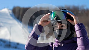 Woman face in a helmet and a mask from cold, frost and wind puts on sunglasses preparing for skiing. Mountaineering ski