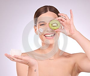 Woman, face and kiwi with moisturizer for skincare nutrition, cream or healthy diet against gray studio background