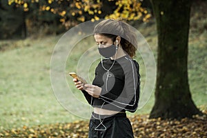 Woman with face mask checking smartphone while jogging