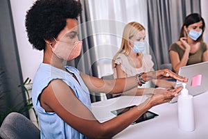 Woman with face mask disinfecting her hands while working in the office during virus epidemic