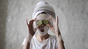 A woman in a face mask is having fun with round cucumbers, looking at the camera and fooling around. Natural