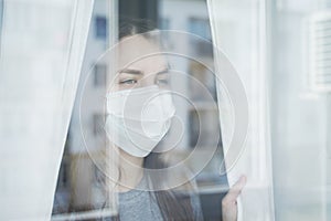 Woman in Face Mask Looking out the Window. Staying Home in Quarantine