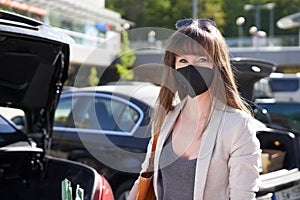 Woman in face mask packing to car trunk