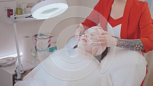 Woman on face mask procedure with cosmetologist in cosmetology clinic.