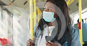 Woman with face mask rides in a public transport bus holding on to a barrier,