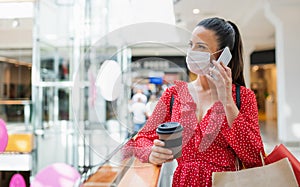Woman with face mask standing and using smartphone indoors in shopping center, coronavirus concept.
