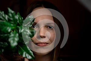 Woman face portrait with green plants on dark background. Attractive woman in her forties. Cosmetology, skin care concept