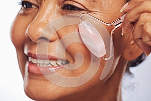 Woman, face roller and massage for skincare, detox dermatology and aesthetic wellness in studio. Closeup of happy mature