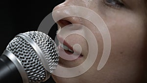 Woman face is singing song into microphone, extreme close up. Female lips with microphone in professional vocal studio. Song produ