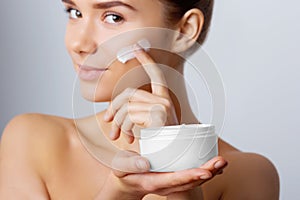 Woman Face Skin Care. Portrait Of Attractive Young Female Applying Cream And Holding Bottle.