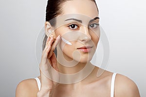 Woman Face Skin Care.  Woman Face Skin Care. Portrait Of Attractive Young Female Applying Cream  And Holding Bottle. Closeup Of