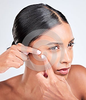 Woman, face and squeeze acne in studio of breakout, dermatology or worry of scar on white background. Indian model check