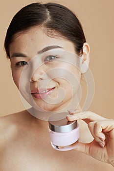 woman with facial cream jar against beige background