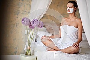 Woman with facial mask doing yoga at morning in bed