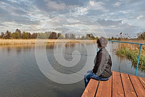 Woman facing at river while sitting on wooden pavement