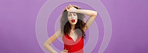 Woman fainting feeling bad whiping sweat of forehead standing drained and exhausted over purple background in red