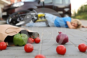 Woman fallen from bicycle after car accident, focus on scattered vegetables