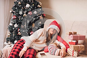 Woman falling asleep and tired of gift wrapping with puppy dog on a couch in the living room with Christmas tree at home