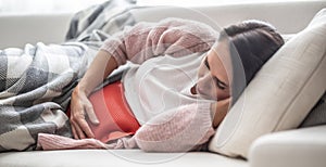 Woman falling asleep under the blanket on a couch after thermophore released the menstruation pain in her belly