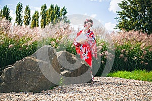 Woman with fancy makeup as Japanese Geisha in garden with a fan