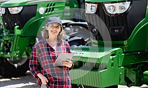 Woman farmer with a digital tablet on the background of an agricultural tractor.s