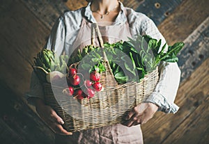 Woman farmer holding basket of fresh vegetables and greens