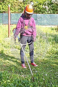 Woman farmer mows the grass in the backyard using string trimmer