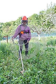 Woman farmer mows the grass in the backyard using string trimmer