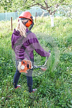 Woman farmer mows the grass in the backyard using string trimmer