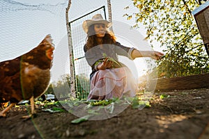 Woman farmer smiling feeding greens to free-range chickens on sunny farm