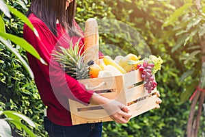 Woman farmer standing hold full fresh food raw vegetables fruit in a wood box