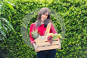 Woman farmer standing hold full fresh food raw vegetables fruit in a wood box