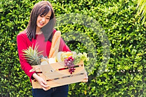 Woman farmer standing hold full fresh food raw vegetables fruit in a wood box